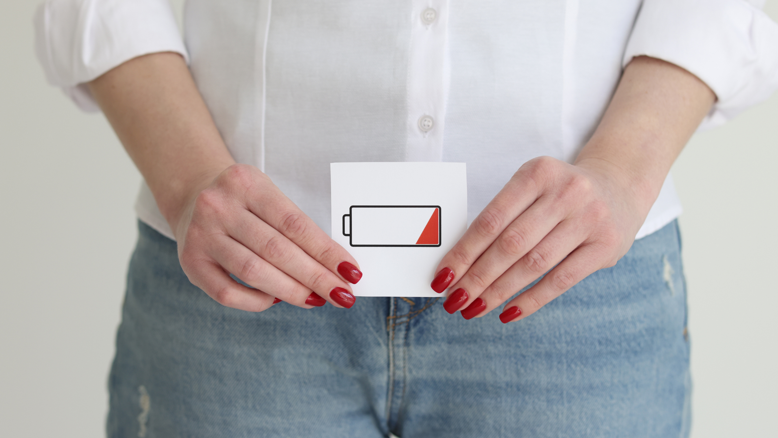 Das Bild zeigt eine Frau, die eine Zeichnung mit einer niedrig gefüllten Batterie vor sich hält. Die Zeichnung ist auf Gürtelhöhe und demonstriert niedrige Libido.